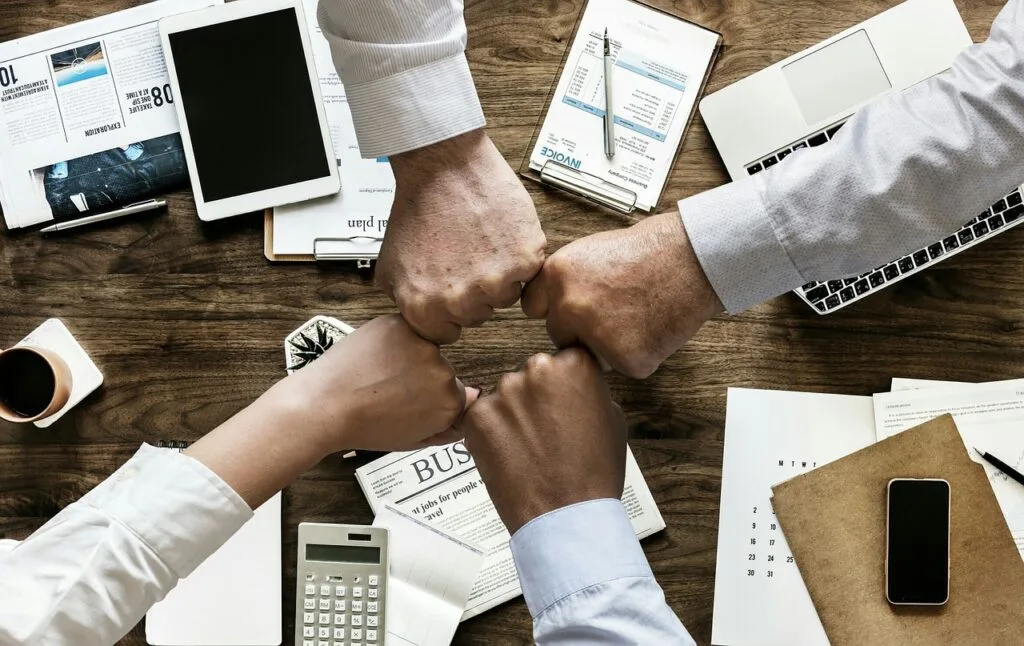 Quatre collègues en fist bump au-dessus d'un bureau avec documents et outils de travail