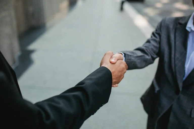 Deux hommes en costume se serrant la main dans la rue